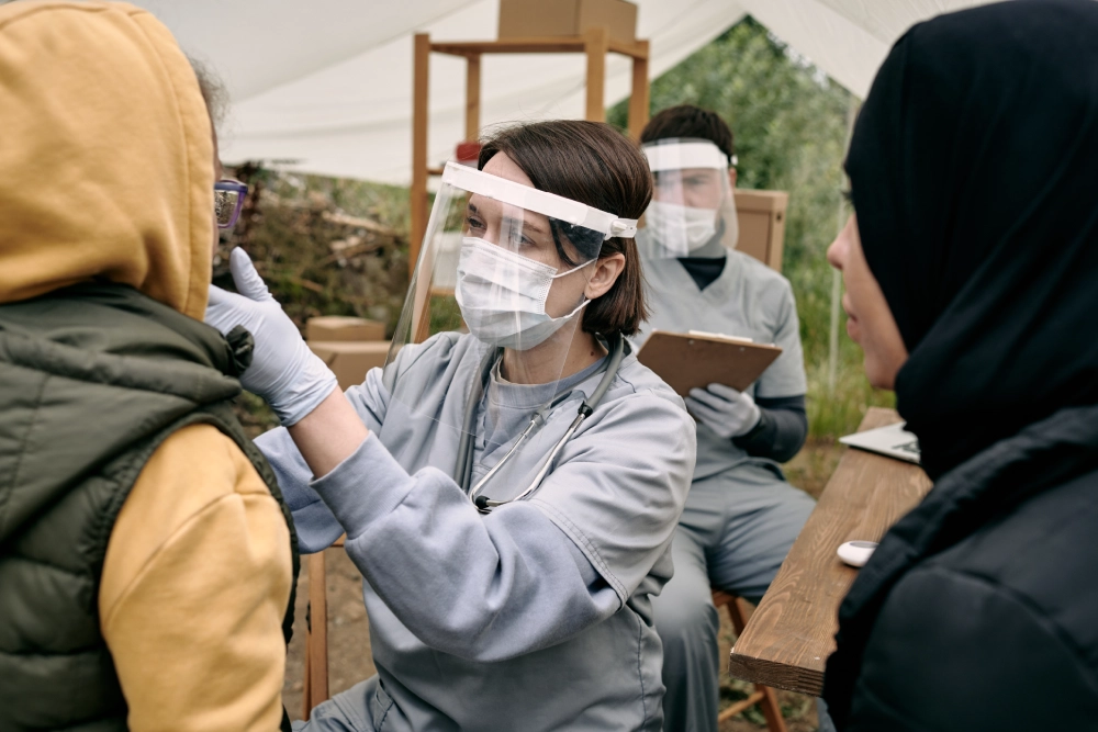 Woman in face shield examines young girl.