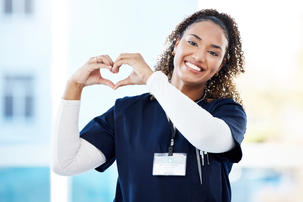 Smiling nurse makes heart shape with hands.