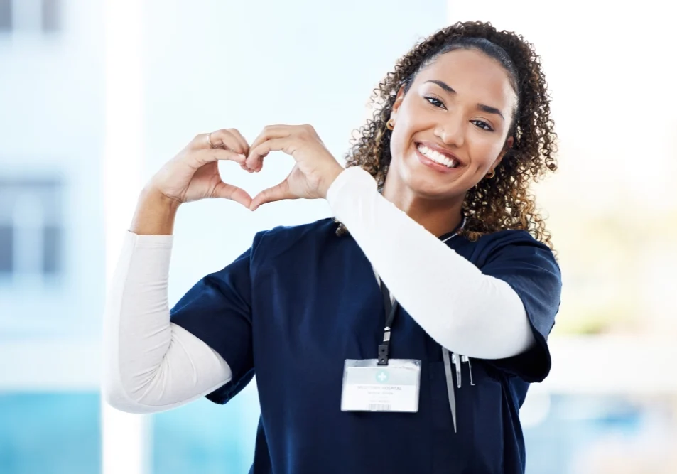 Smiling nurse makes heart shape with hands.
